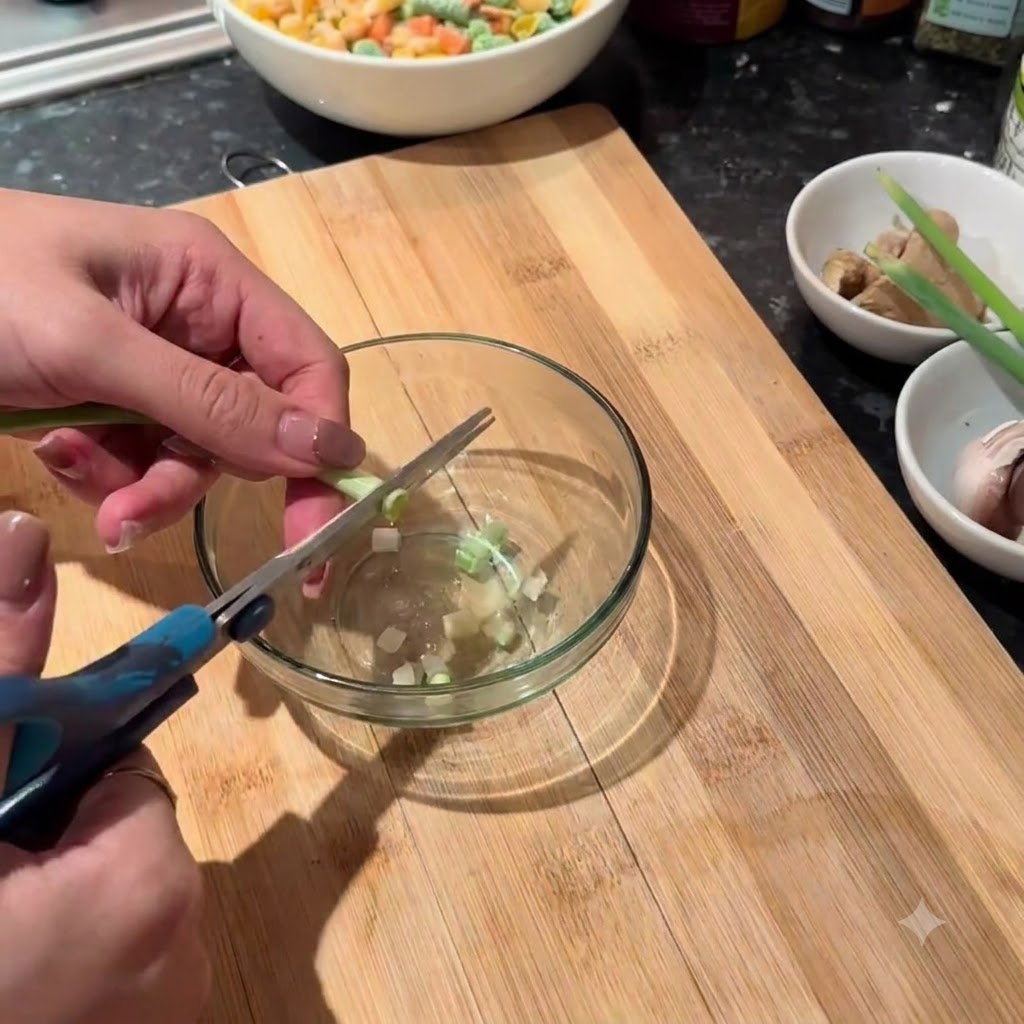 Tiges de ciboulette verte coupées en petits morceaux avec des ciseaux dans un bol en verre.