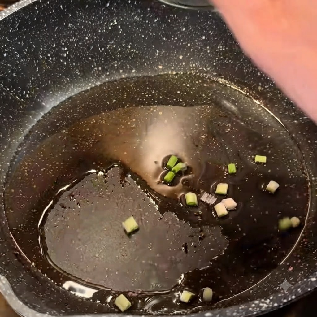 Oignons verts hachés grésillant dans de lhuile chaude à lintérieur dune poêle sombre.