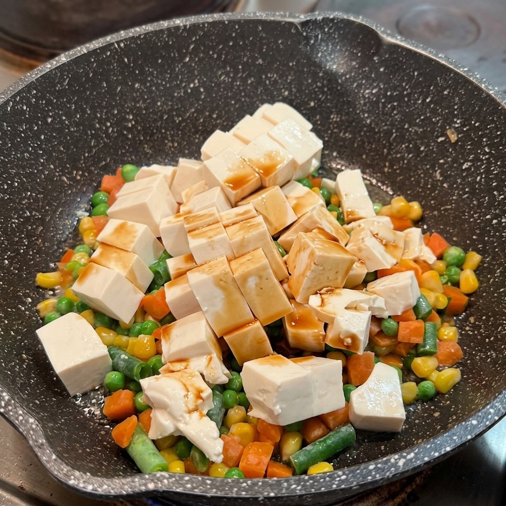 Sauce soja répartie sur les cubes de tofu soyeux et les légumes mélangés dans une poêle.