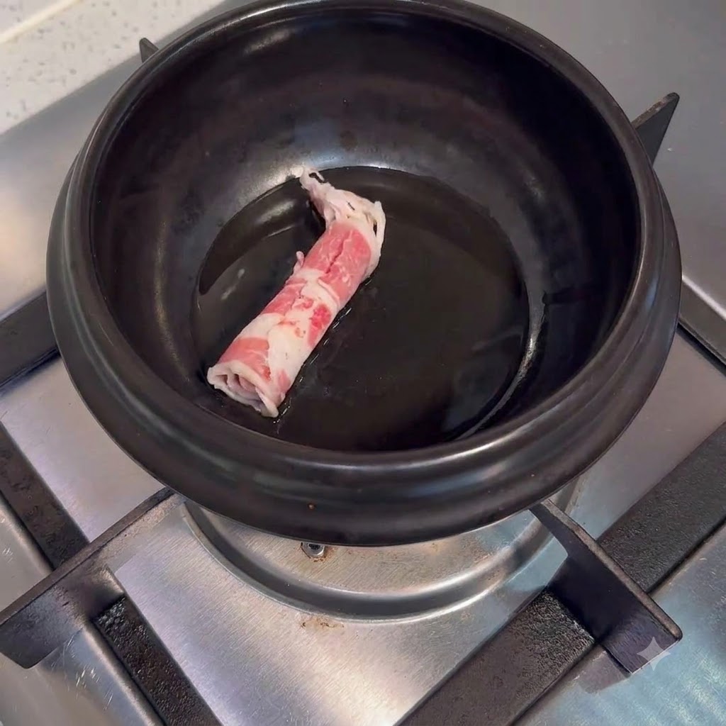 Tranches de bœuf crues placées dans un pot de cuisson en céramique noire avec de lhuile sur un brûleur de cuisinière.