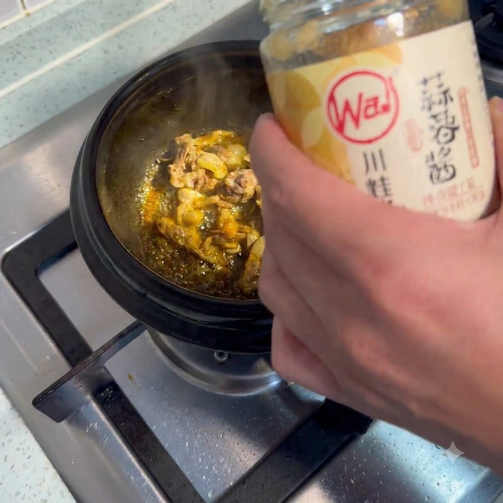 Une cuillerée de purée dail prélevée et ajoutée dans une casserole de viande grésillante.