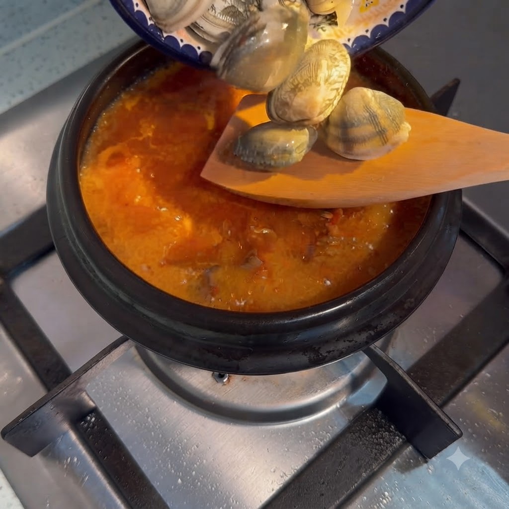 Palourdes fraîches versées dune petite assiette dans une casserole bouillante de soupe coréenne au tofu soyeux.