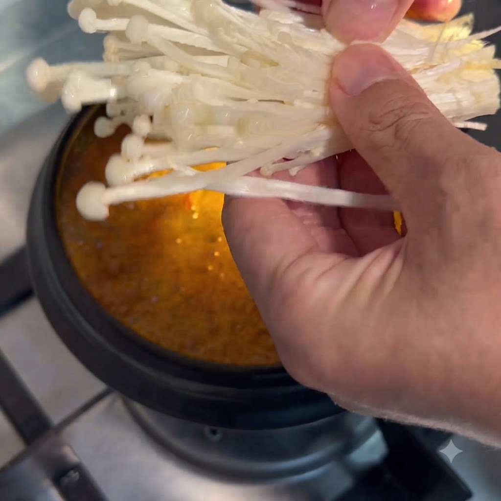 Champignons enoki tenus à la main et abaissés dans la casserole de soupe mijotante.