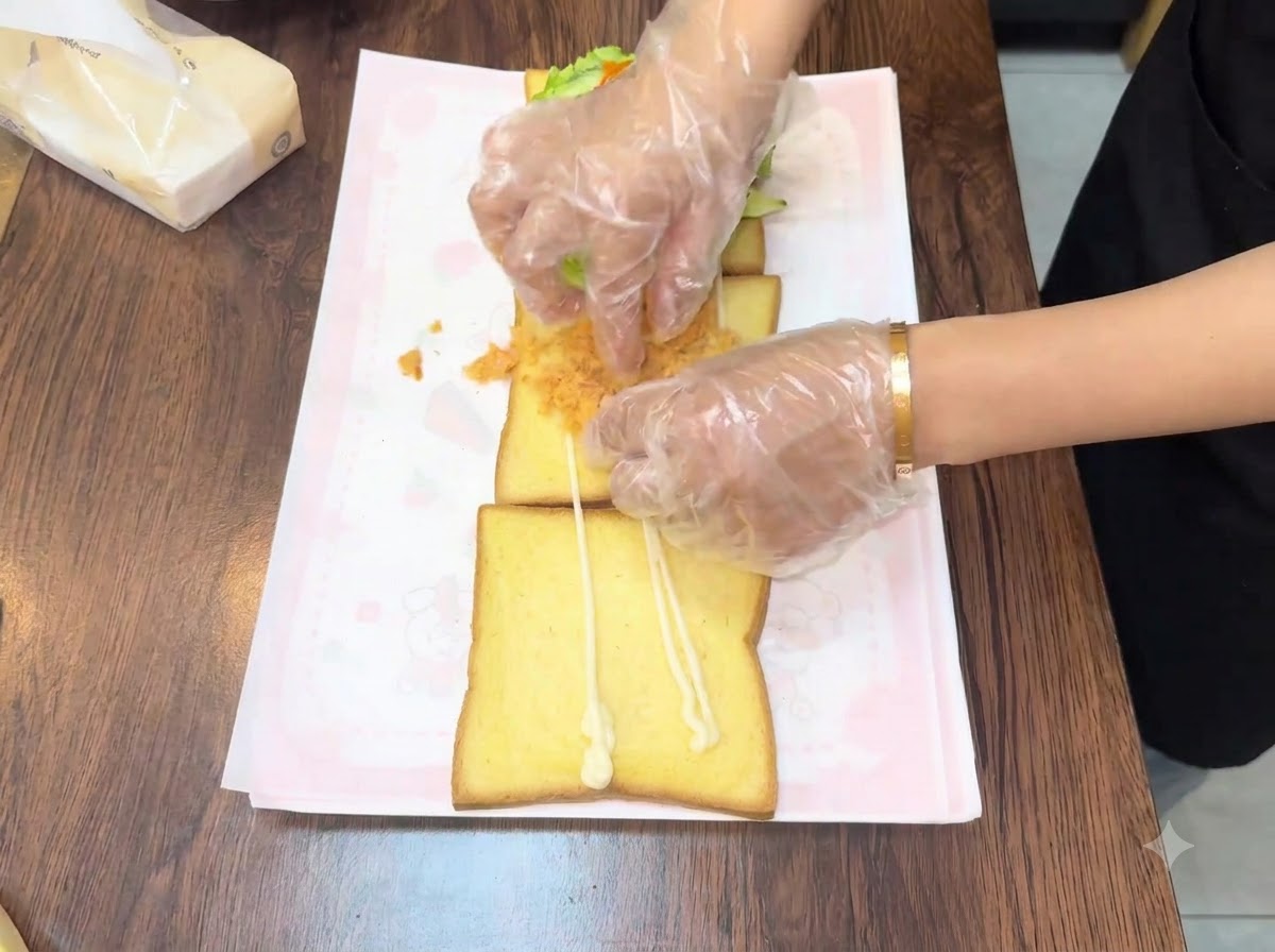 Des mains étalant du floss de viande doré et duveteux sur la deuxième tranche de pain.