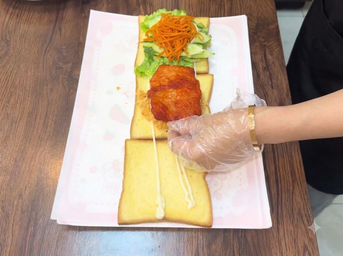 Une main gantée plaçant une escalope de poulet frite et chaude sur lassemblage.