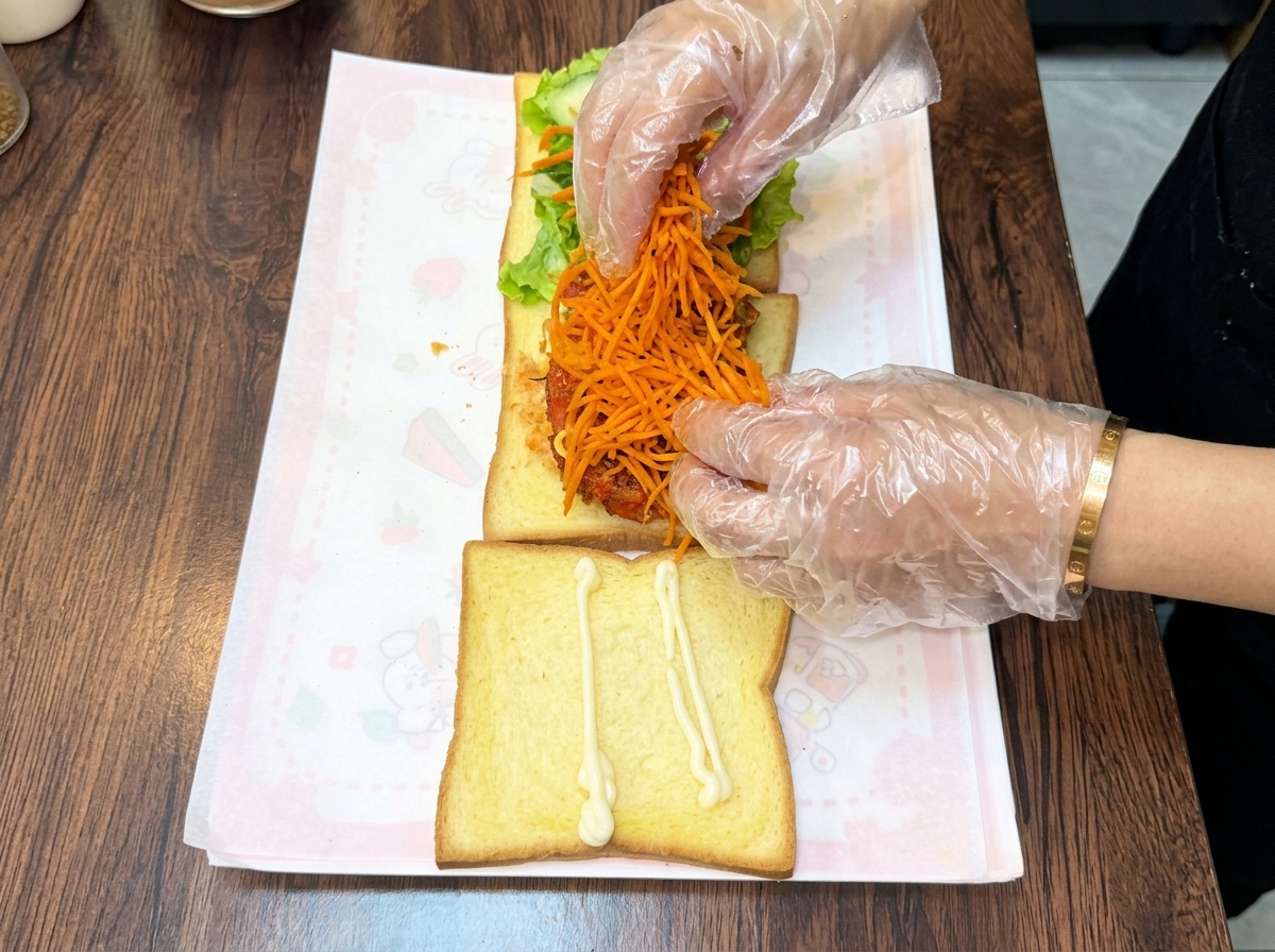 Des mains gantées empilant un monticule de carottes râpées orange sur lescalope de poulet.