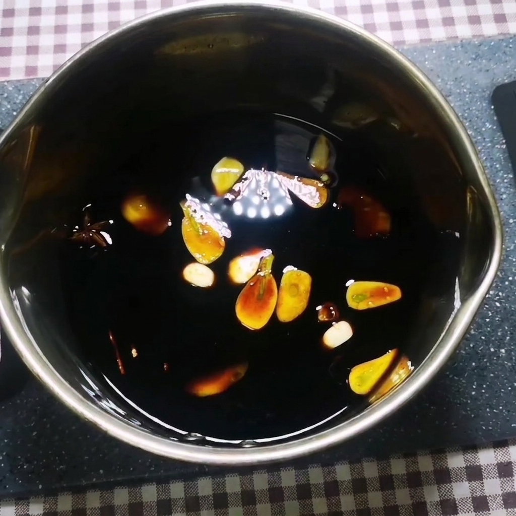 Une sauce foncée mijotant dans une casserole en métal avec de lail, du gingembre, de lanis étoilé et de la cannelle flottant à lintérieur.
