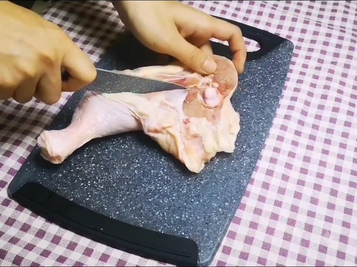 Un couteau bien aiguisé longeant los dune cuisse de poulet crue sur une planche à découper pour en retirer los.