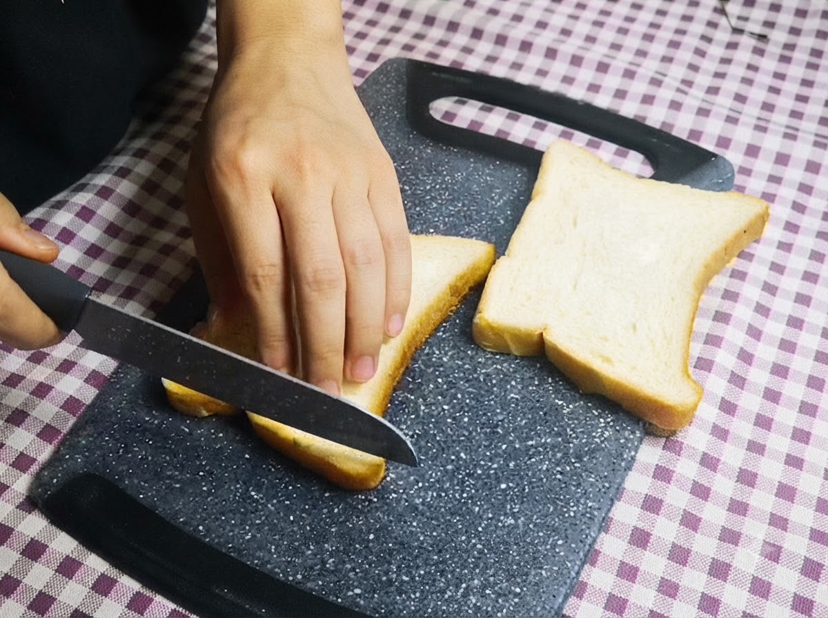 Une personne utilisant un couteau pour couper les croûtes de tranches de pain blanc sur une planche à découper.