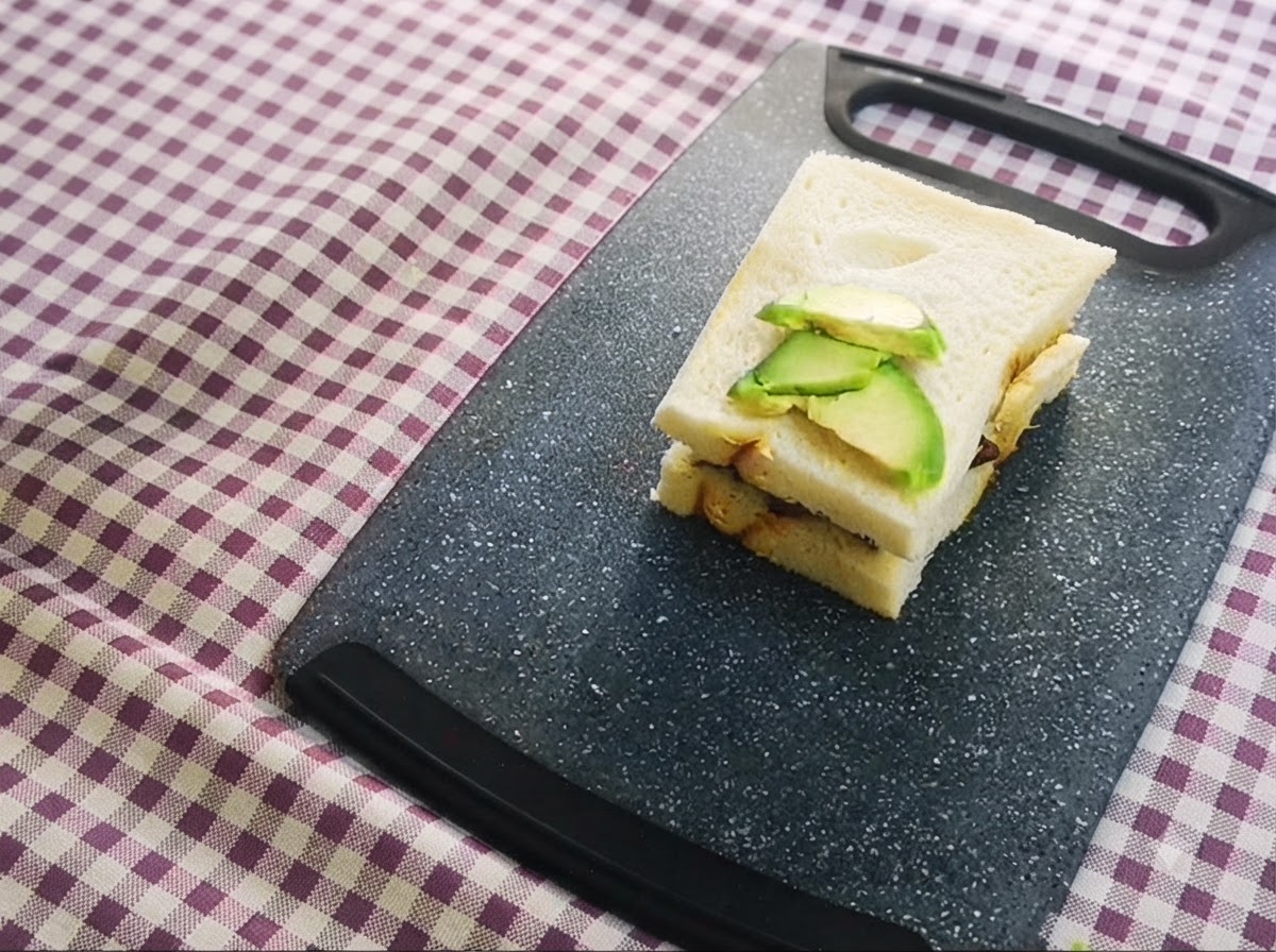 Un sandwich en couches garni de tranches davocat sur le dessus, reposant sur une planche à découper.