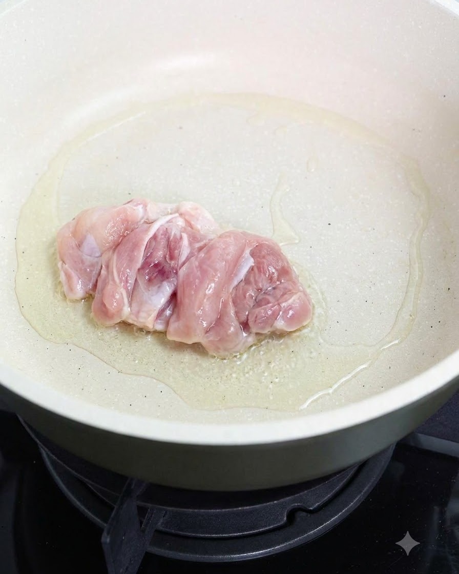 Un haut de cuisse de poulet cru en train de frire côté peau dans une poêle huilée.