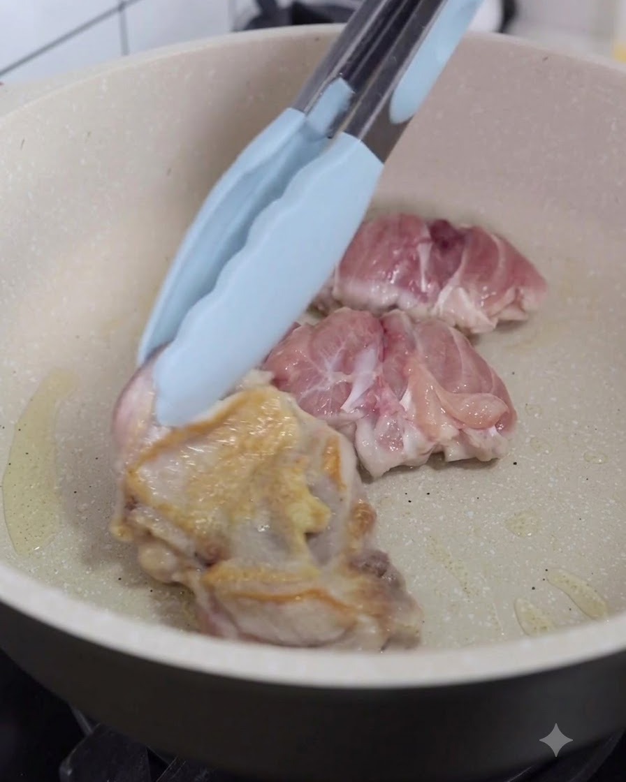 Morceaux de poulet retournés dans la poêle à laide de pinces de cuisine.