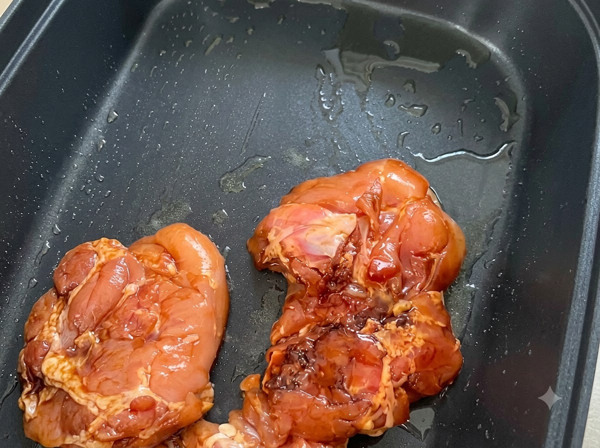 Morceaux de poulet marinés disposés côté peau dans une poêle antiadhésive noire graissée.