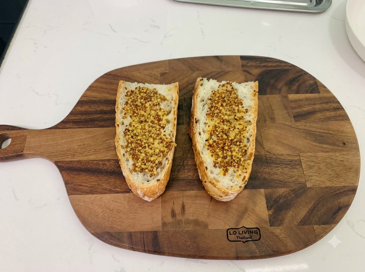 Deux tranches de pain rustique disposées sur une planche à découper en bois, généreusement tartinées de moutarde à lancienne.