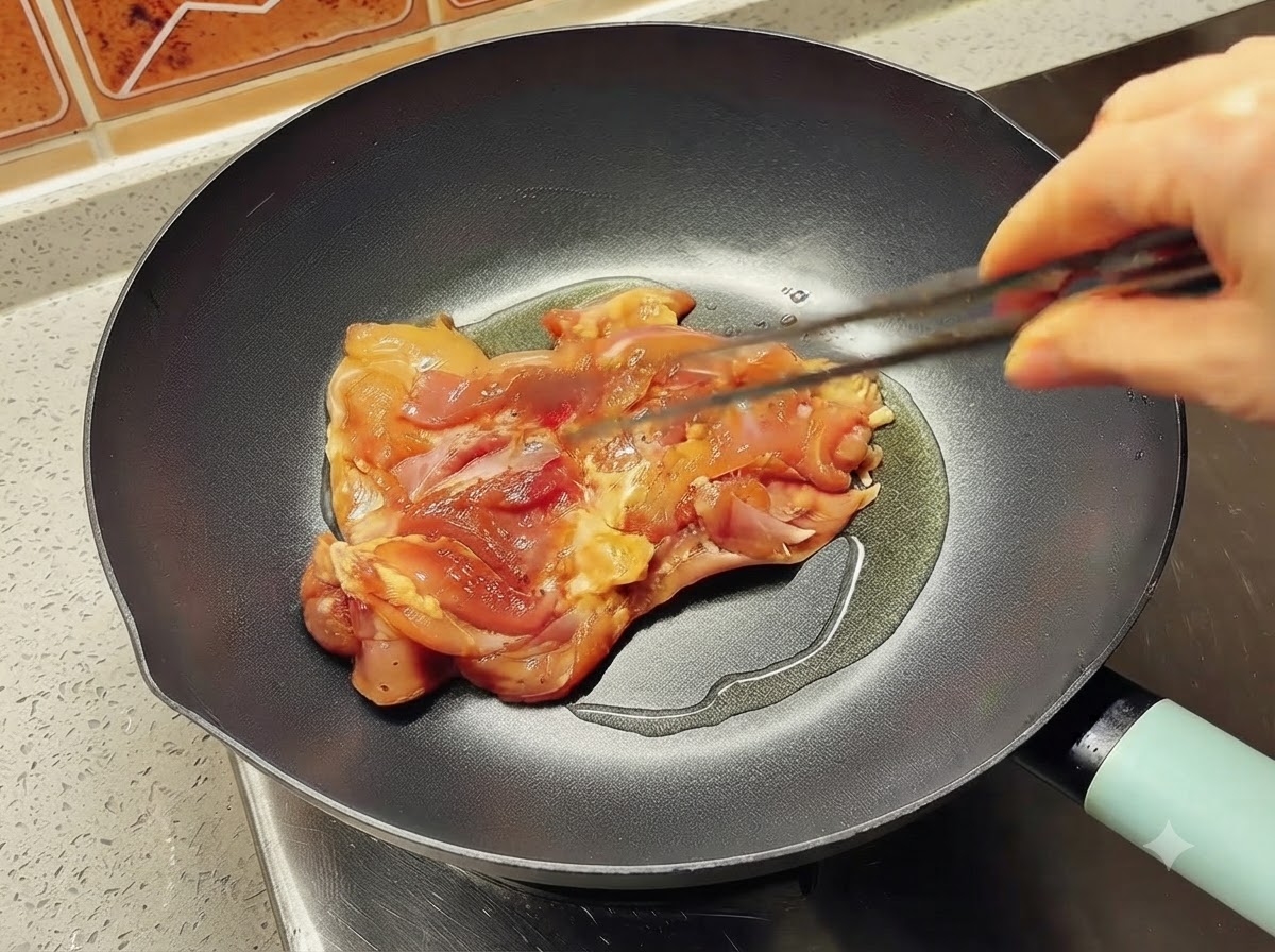 Un morceau de cuisse de poulet mariné déposé dans une poêle huilée et chaude à laide de pinces.