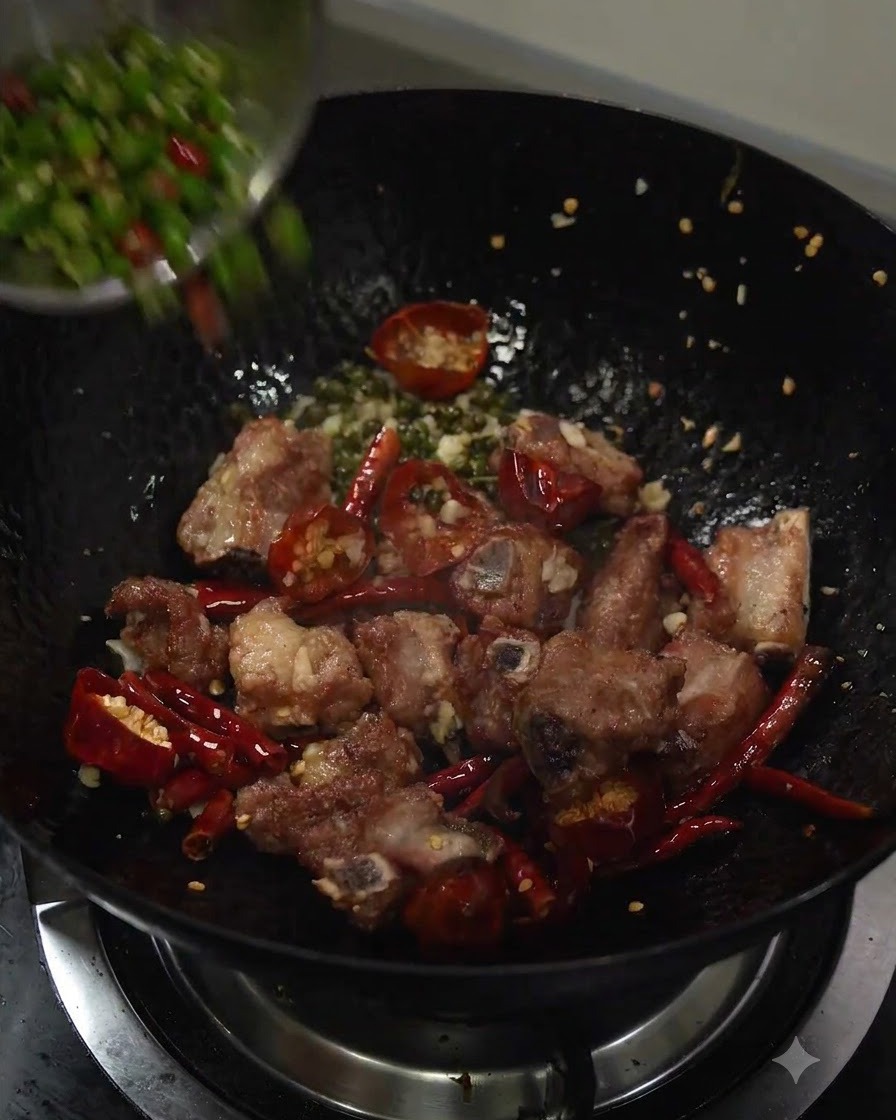 Piments verts émincés versés dans le wok avec les travers de porc sautés et les aromates.