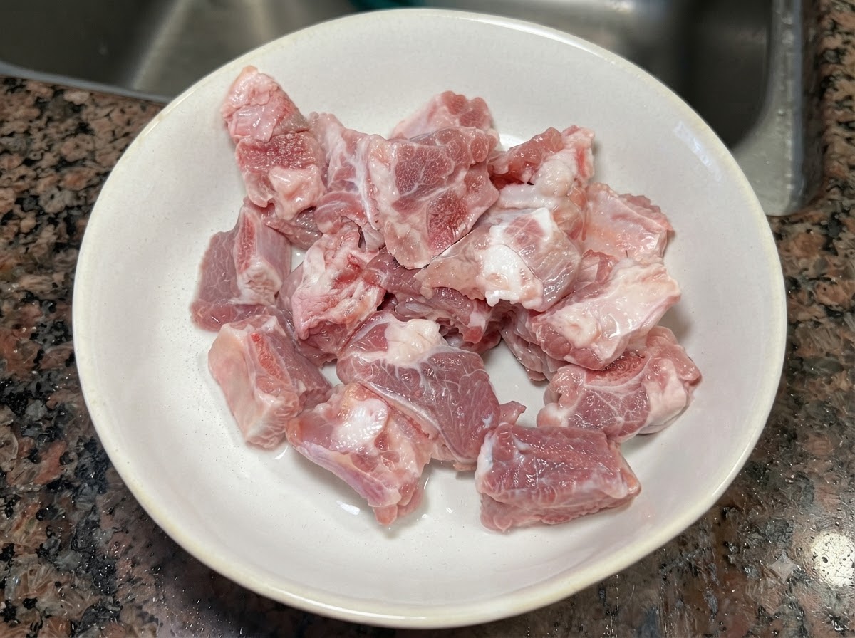 Morceaux de travers de porc crus frais reposant dans un bol en céramique blanc.