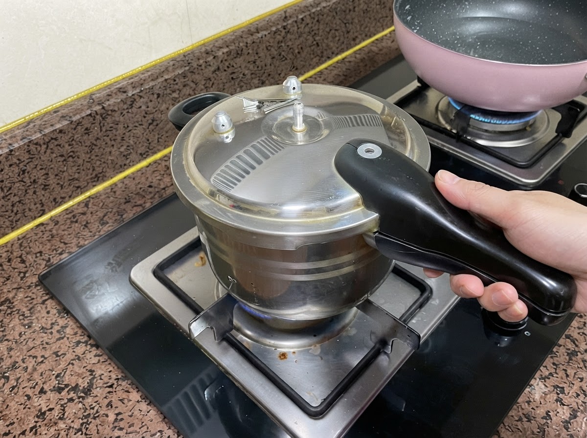 Couvercle dautocuiseur fermé sur un brûleur de cuisinière avec une main saisissant la poignée.