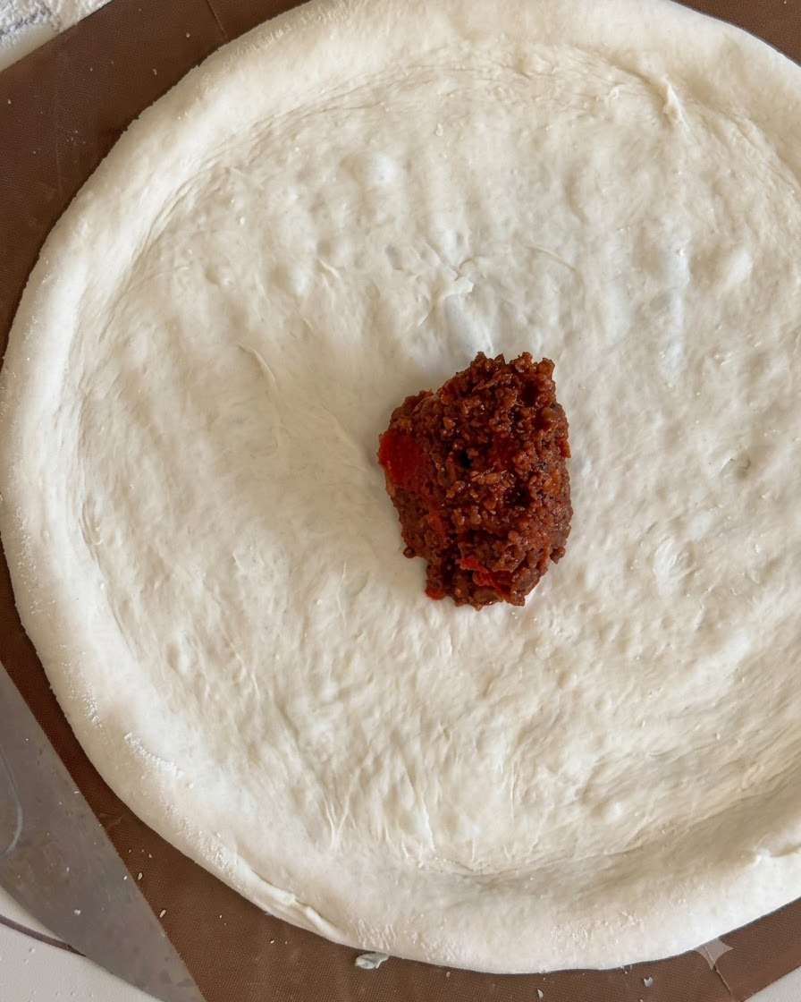 Une petite quantité de sauce à la viande rouge au centre dune pâte à pizza.