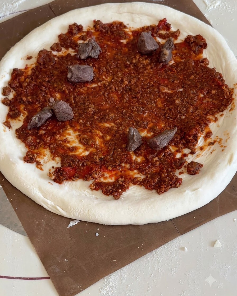 Morceaux dananas et de bœuf répartis sur la base de pizza à la sauce tomate.