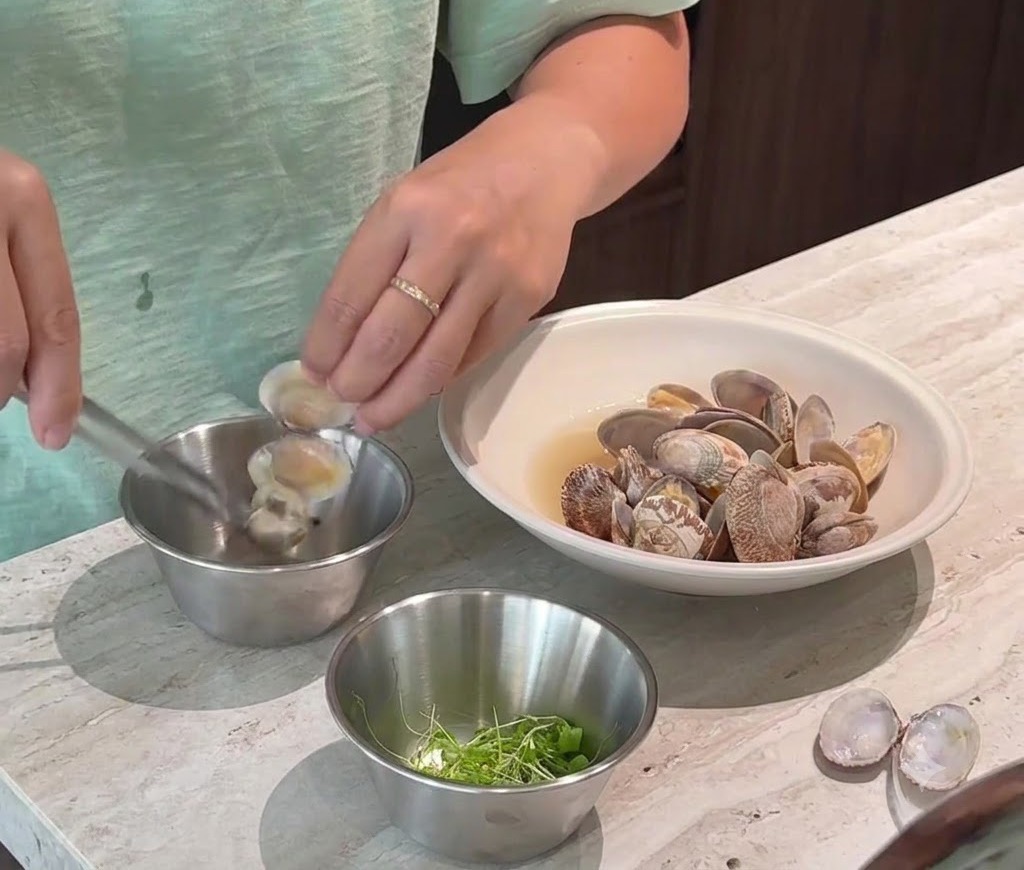 Une personne retirant délicatement la chair des palourdes cuites hors de leurs coquilles pour la placer dans un petit bol en métal.