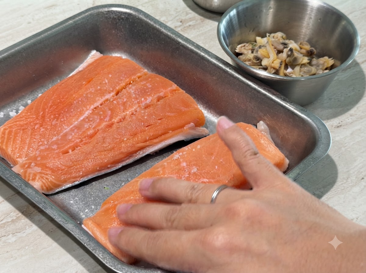 Une main pressant légèrement du sel et du poivre noir sur des filets de saumon crus.