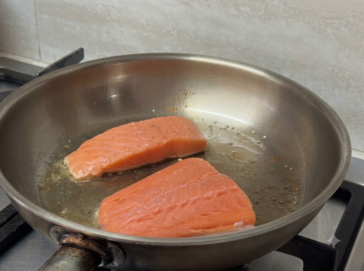 Deux filets de saumon en train de grésiller et de dorer dans une poêle chaude.