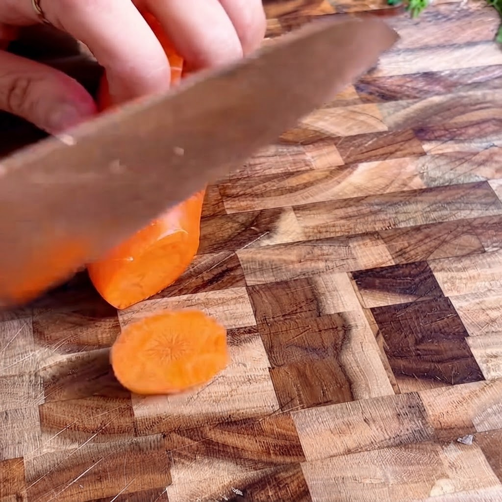 Des rondelles de carotte rangées proprement sur une planche à découper en bois.