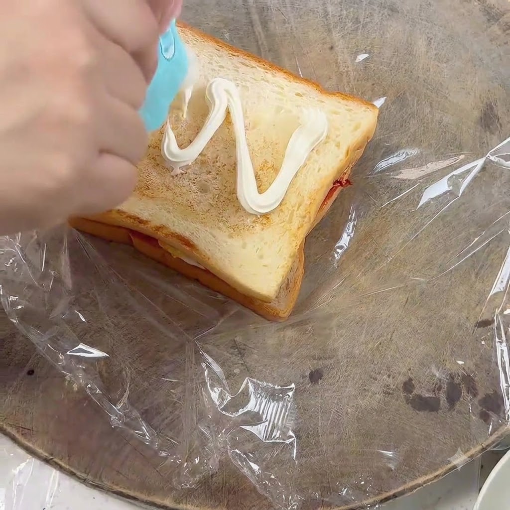 Presser de la mayonnaise en motif de zigzag sur une tranche de pain toasté.