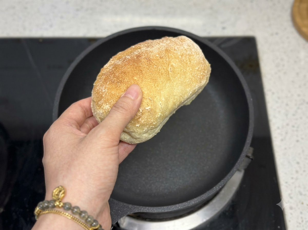 Une main tenant un pain ciabatta directement au-dessus dune poêle à frire noire vide.