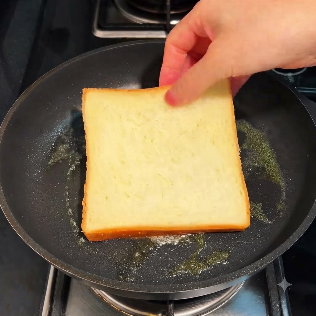 Une tranche de pain de mie en train de griller dans une poêle avec du beurre à feux doux.
