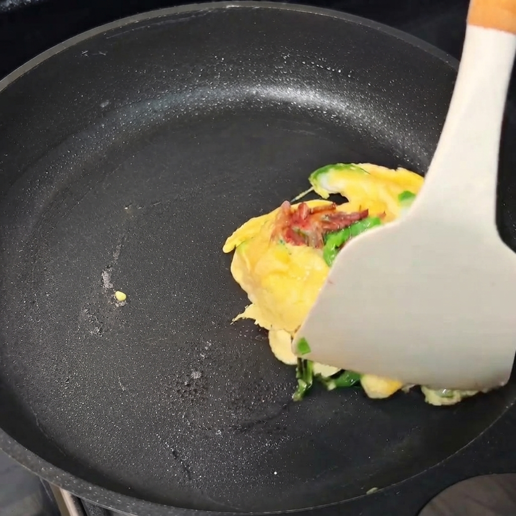Une omelette en cours de pliage avec une spatule à lintérieur dune poêle.