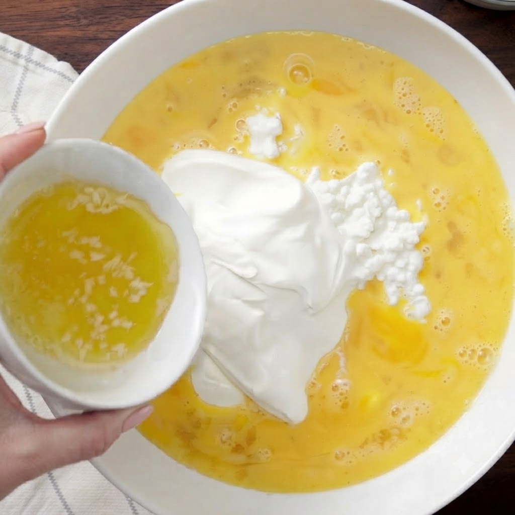 Du beurre fondu versé dun petit bol blanc dans le bol mélangeur.