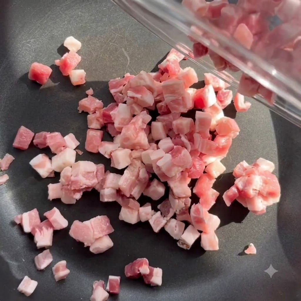Morceaux de lard en dés cuisant et fondant dans une poêle noire à feu moyen.