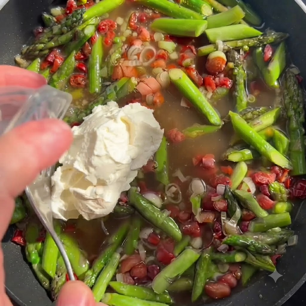 Une cuillerée de fromage mascarpone blanc ajoutée au bouillon et aux légumes dans une poêle.