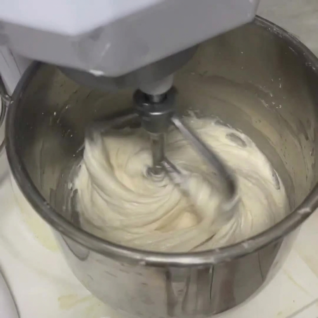 Pâte blanche se combinant avec le liquide à lintérieur dun grand bol de robot pâtissier en acier inoxydable à laide dun crochet pétrisseur.