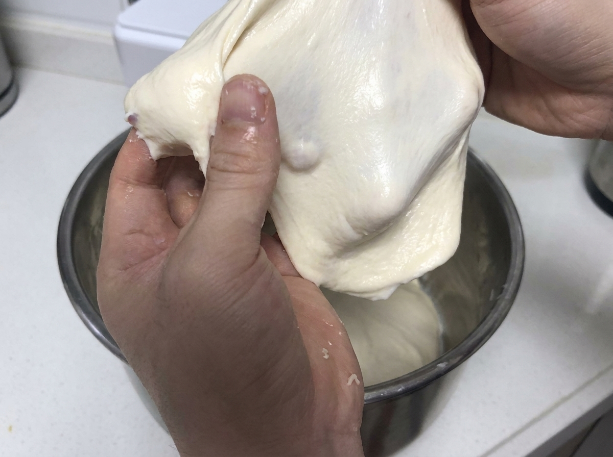 Mains tirant et étirant un morceau souple de pâte blanche élastique pour démontrer la force du gluten.