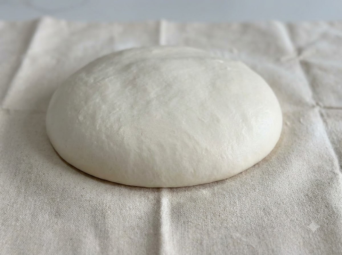 Un dôme lisse et arrondi de pâte blanche posé sur la surface dun linge blanc fariné.