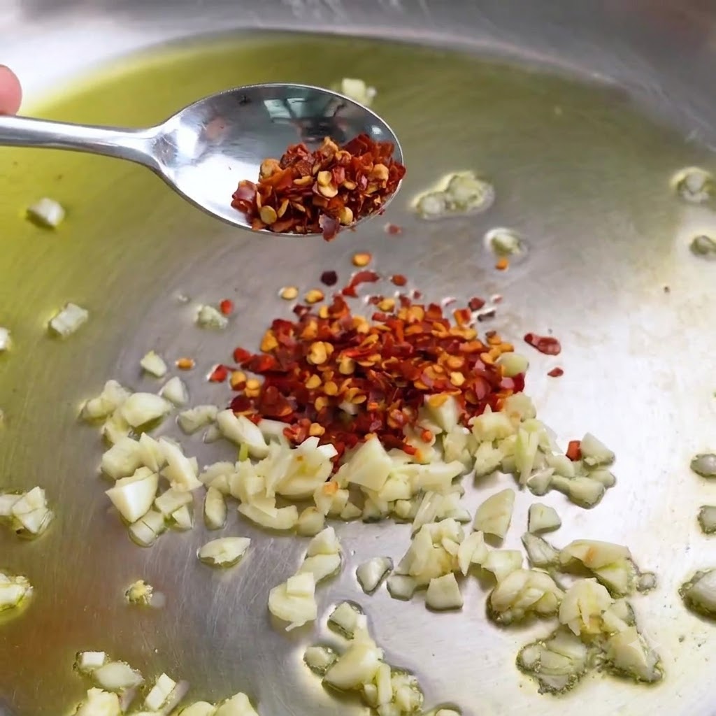 De lail émincé et des flocons de piment grésillant dans une poêle en acier inoxydable avec de lhuile dolive.