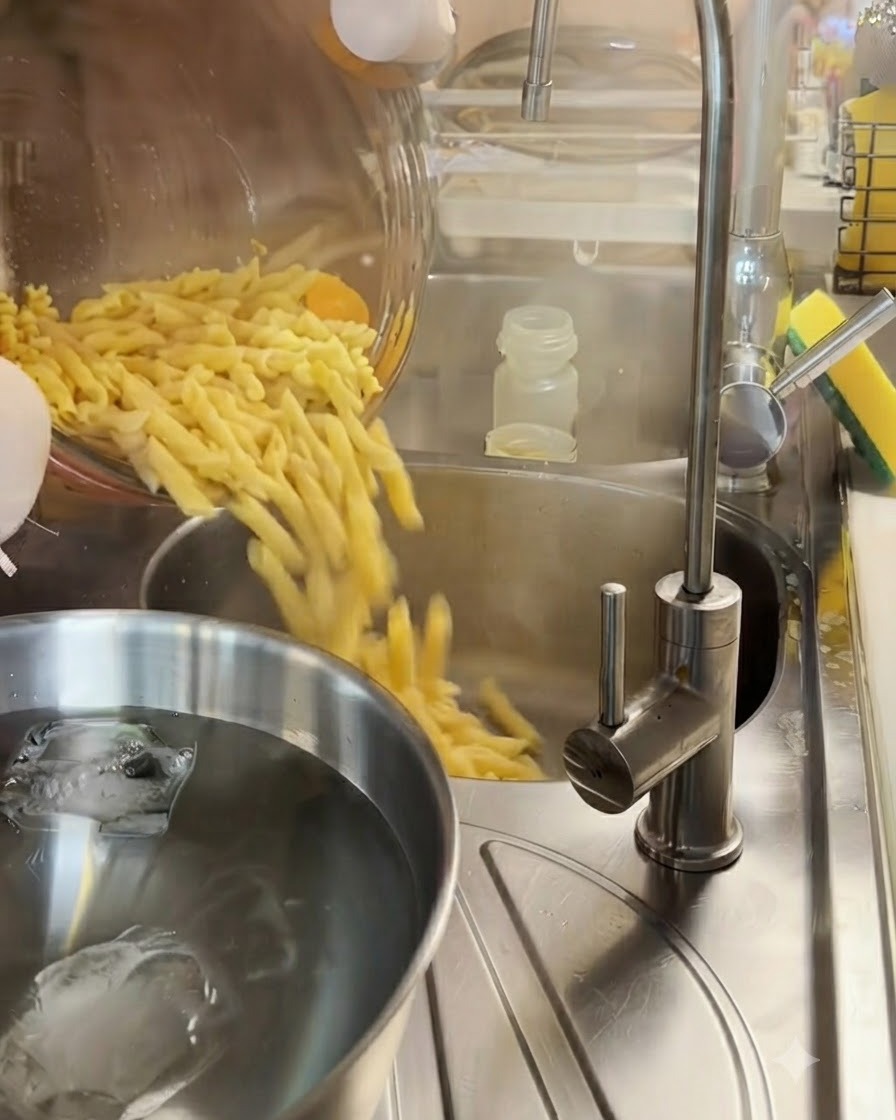 Des pâtes fusilli cuites égouttées dans une passoire en métal au-dessus dun bol deau glacée.