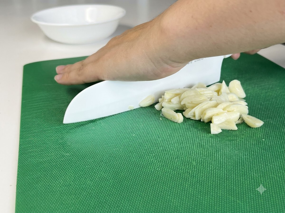 Des gousses dail hachées finement sur une plancha à laide dun couteau blanc.