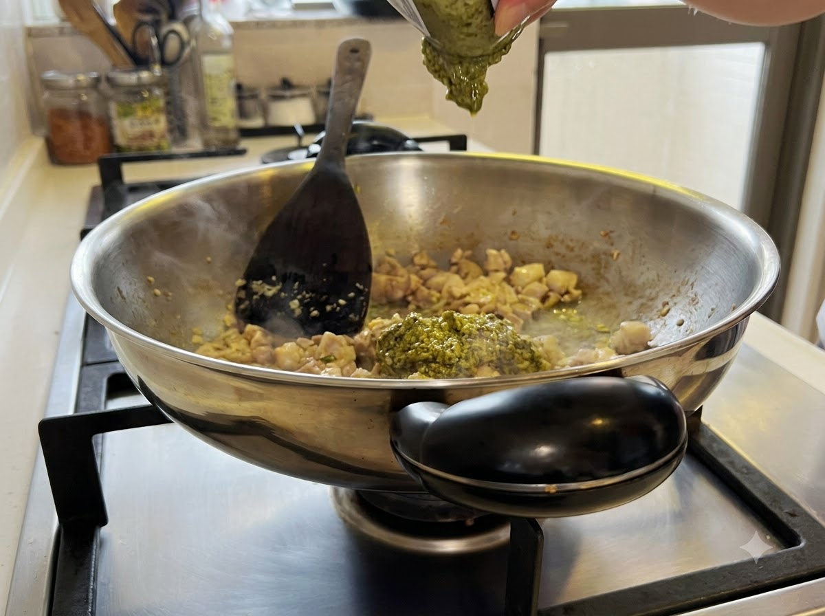 De la sauce pesto vert mélangée au mélange de poulet et dail à lintérieur du wok.