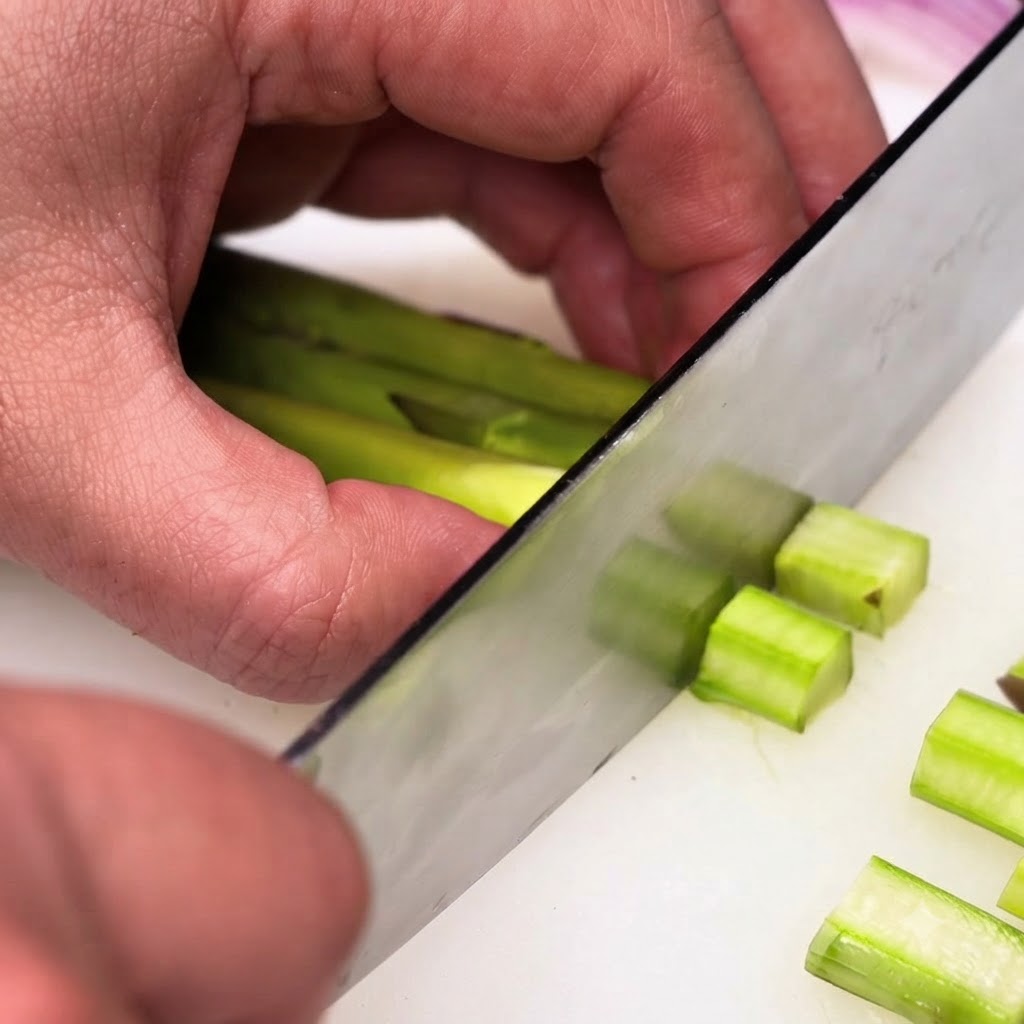 Tiges dasperges vertes épluchées coupées en petits morceaux réguliers à laide dun couteau de chef.