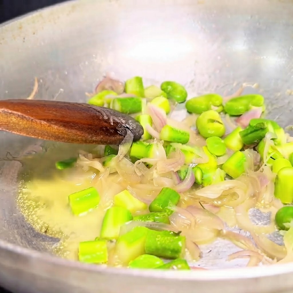 Oignons sautés et légumes verts prélevés dans une poêle en métal avec une cuillère en bois.