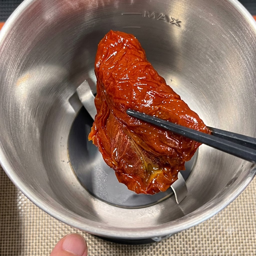 Un morceau de tomate séchée en train dêtre placé dans le bol dun robot culinaire en acier inoxydable à laide de baguettes.