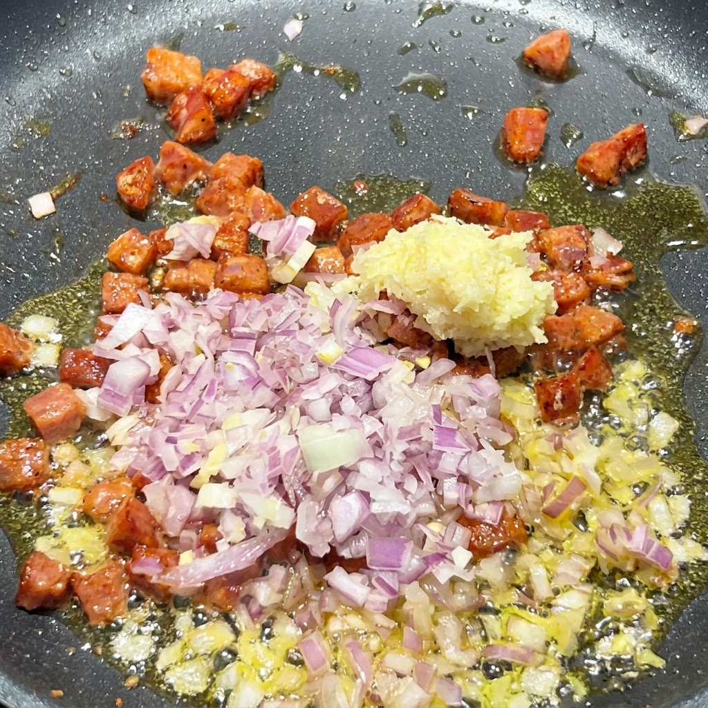 Oignon rouge en dés et ail haché ajoutés dans la poêle grésillante contenant les morceaux de chorizo dorés.