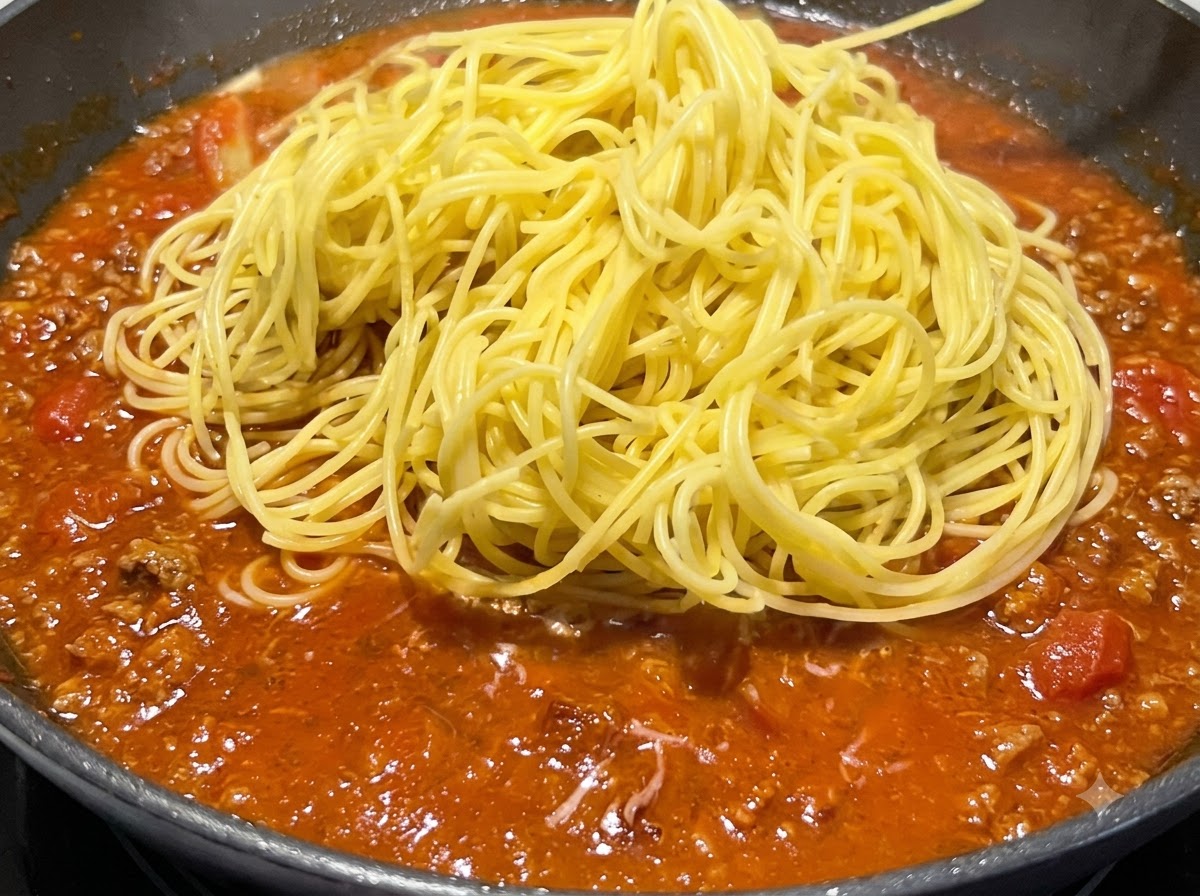 Une portion de spaghettis jaunes cuits disposée sur le dessus de la sauce rouge frémissante dans une poêle.