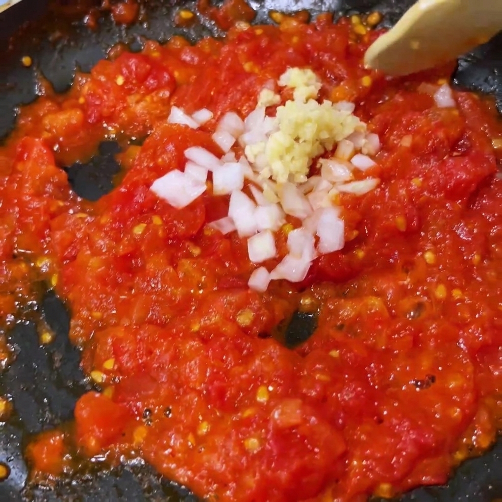 Ail haché et oignon blanc mélangés aux tomates concassées attendries dans une poêle.