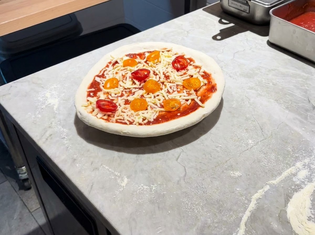 Une pizza entièrement assemblée reposant sur une pelle en métal sur un plan de travail en marbre.