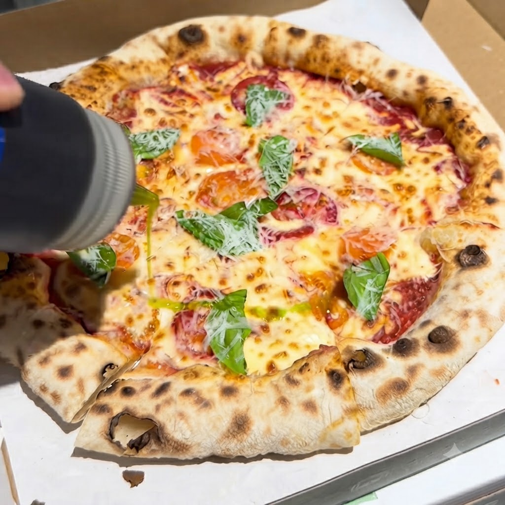 Une bouteille versant un filet dhuile dolive extra vierge sur une pizza fraîchement cuite garnie de basilic et de fromage dans une boîte.